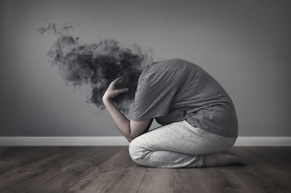 O persoană care stă pe podea cu fum care iese din cap, reprezentând luptele pe care le are cu depresia.