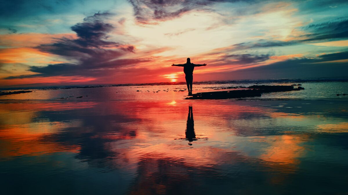 O persoană care stă pe plajă la apus, bucurându-se de frumusețea senină a culorilor naturii care se îmbină armonios